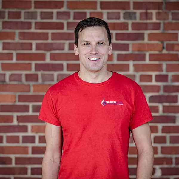 smiling man in red shirt in front of brick wall